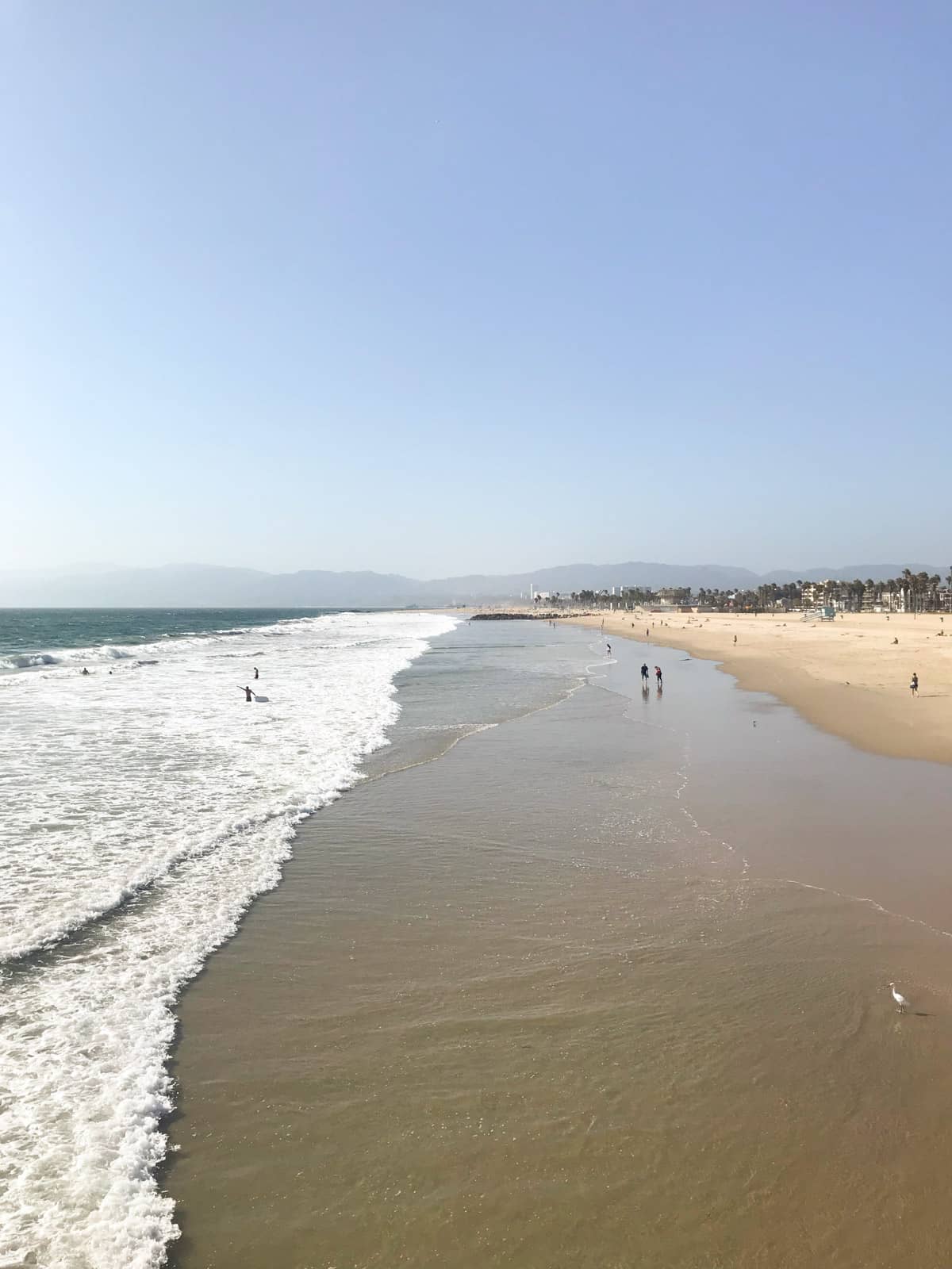 A new of a beach from a boardwalk, where you can see the sea and the sand, much of which has been wet by the sea.