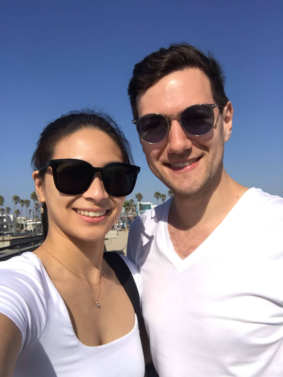 A selfie of a man and woman, both wearing white shirts and both wearing sunglasses