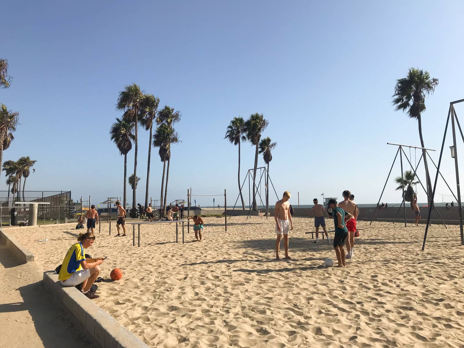 An outdoor beach gym with some equipment, and some people dressed in swimwear using the equipment