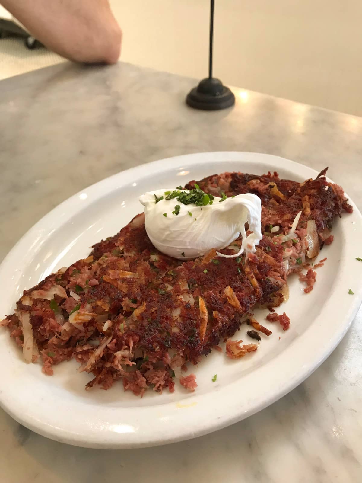 A plate of cooked corned beef and potato roost, served on a white plate with a poached egg on top