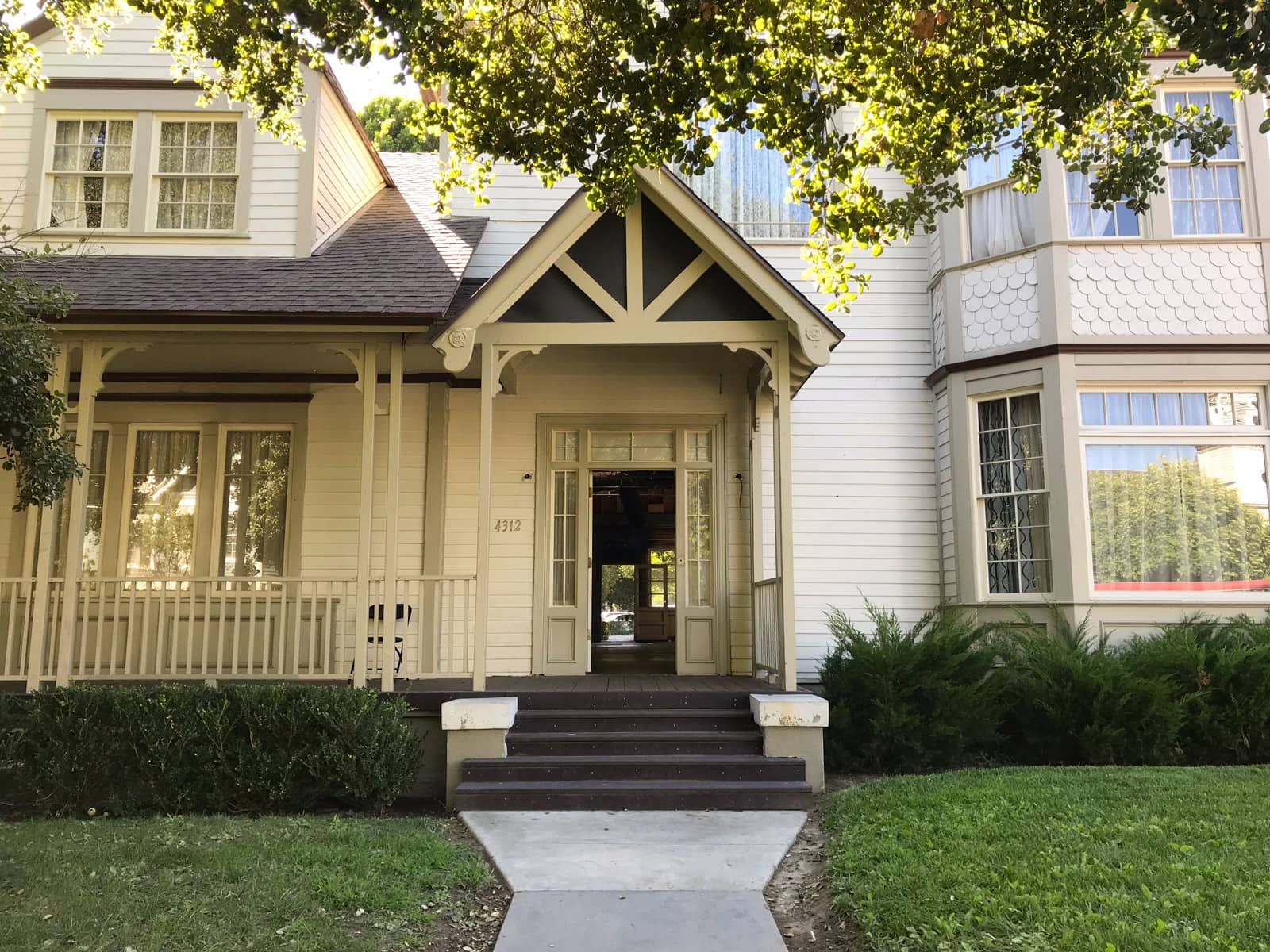 The front of a beige coloured house with a front porch. Some trees leaves can be seen from the top. The area is well shaded