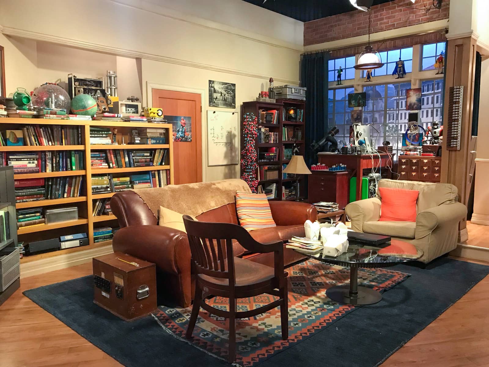 A television stage set up to look like a small apartment, with bookshelves full of books and a window looking out to the city.