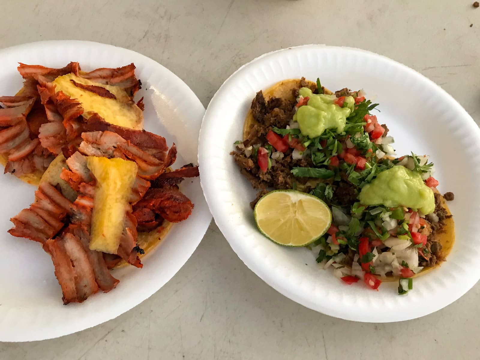 Two plates of tacos; one with pineapple and pork and the other with beef, pico de gallo and guacamole