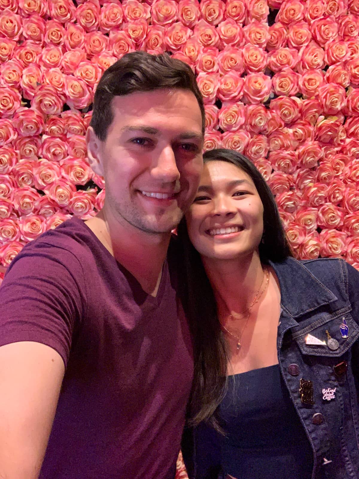 A selfie of a man and woman in front of a backdrop of a makeshift wall of roses
