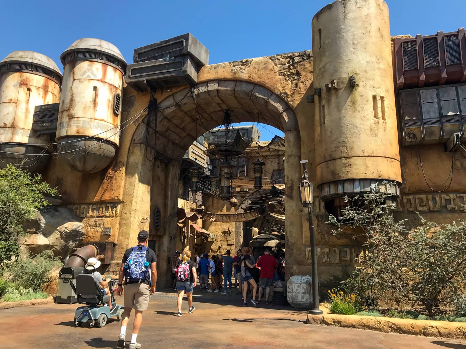 The entrance to an area of a theme park, looking like a castle with turrets. Lanterns and cables suspend from the pillars.