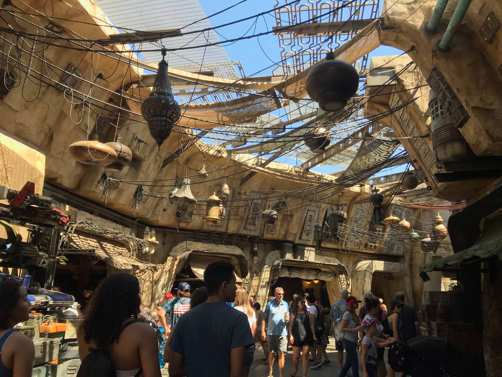 The inside of the area of a theme park with an industrial, old style. Many cables and lanterns hang from the ceiling