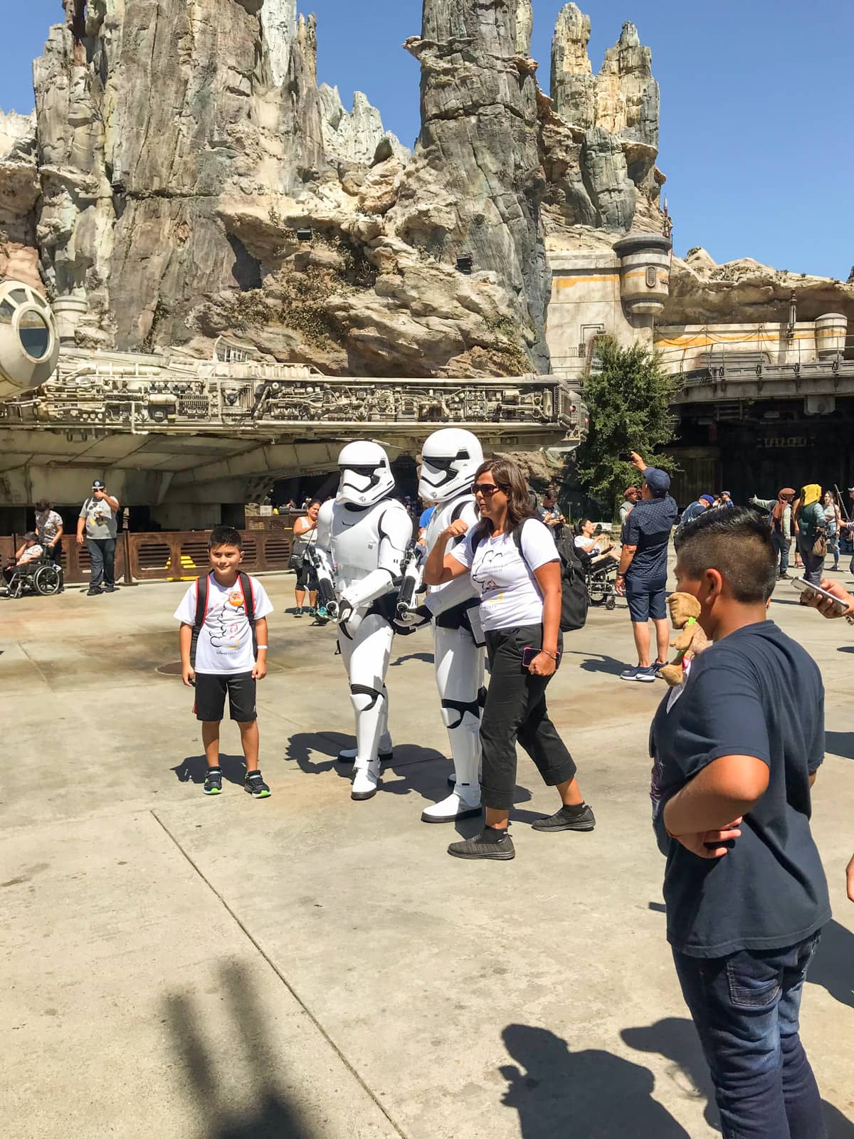 People dressed up in white astronaut-like costumes to resemble Stormtrooper characters from Star Wars, in a theme park with several people surrounding them to take photos with them