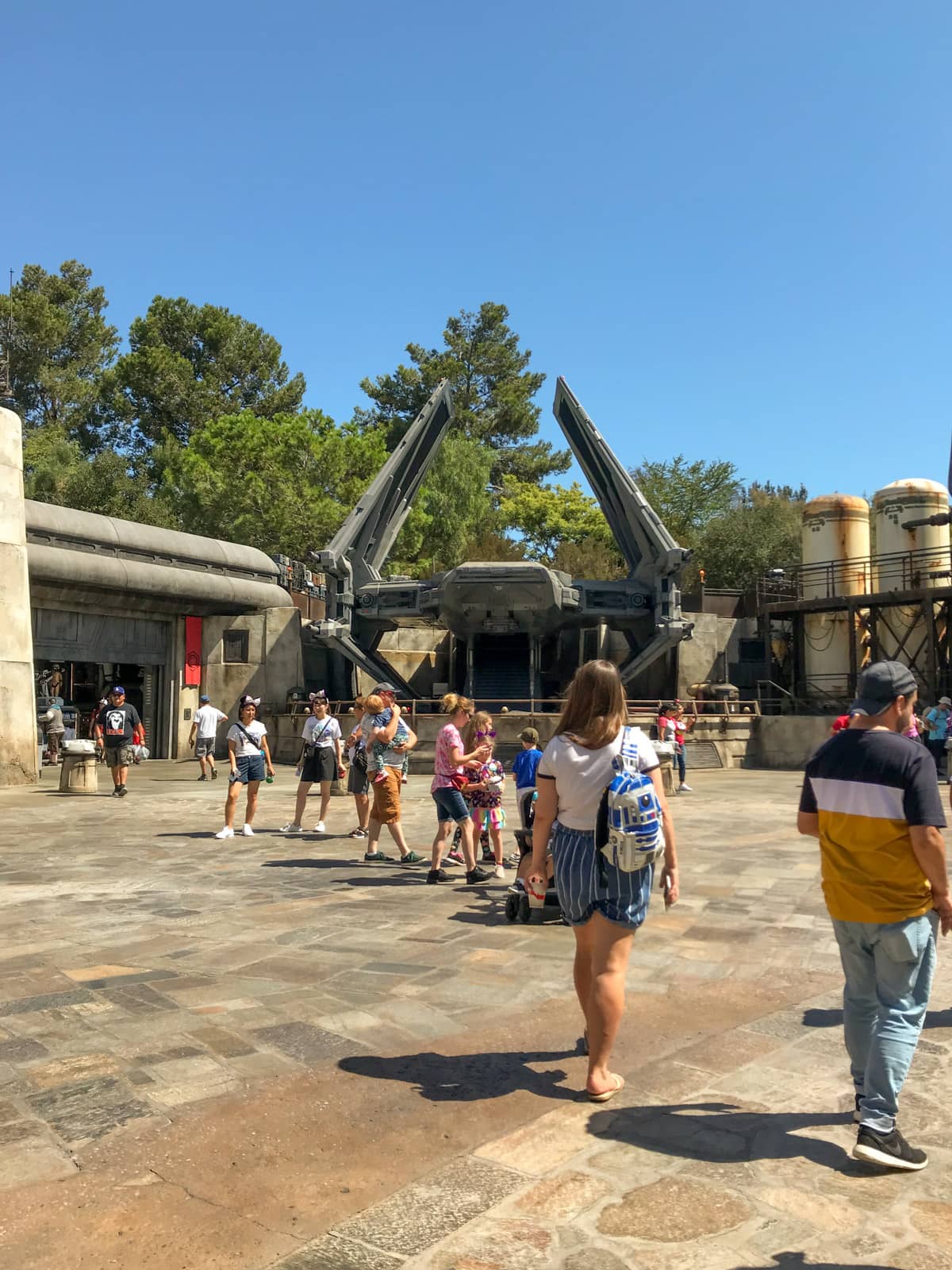 Some people walking around in an open area of a theme park, that is themed to look like a futuristic and earthy outer-space area.