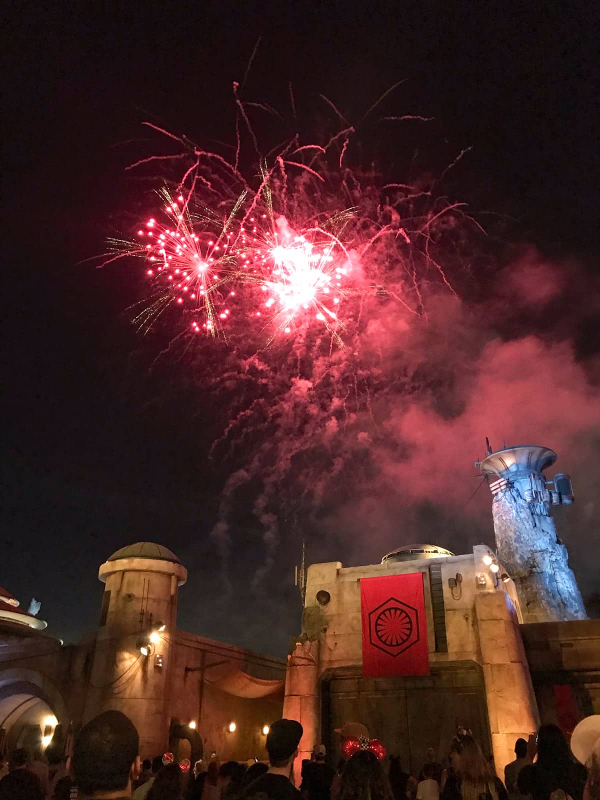 Small pink fireworks across the night sky, seen from an amusement park. The angle of the shot is from the ground upwards.