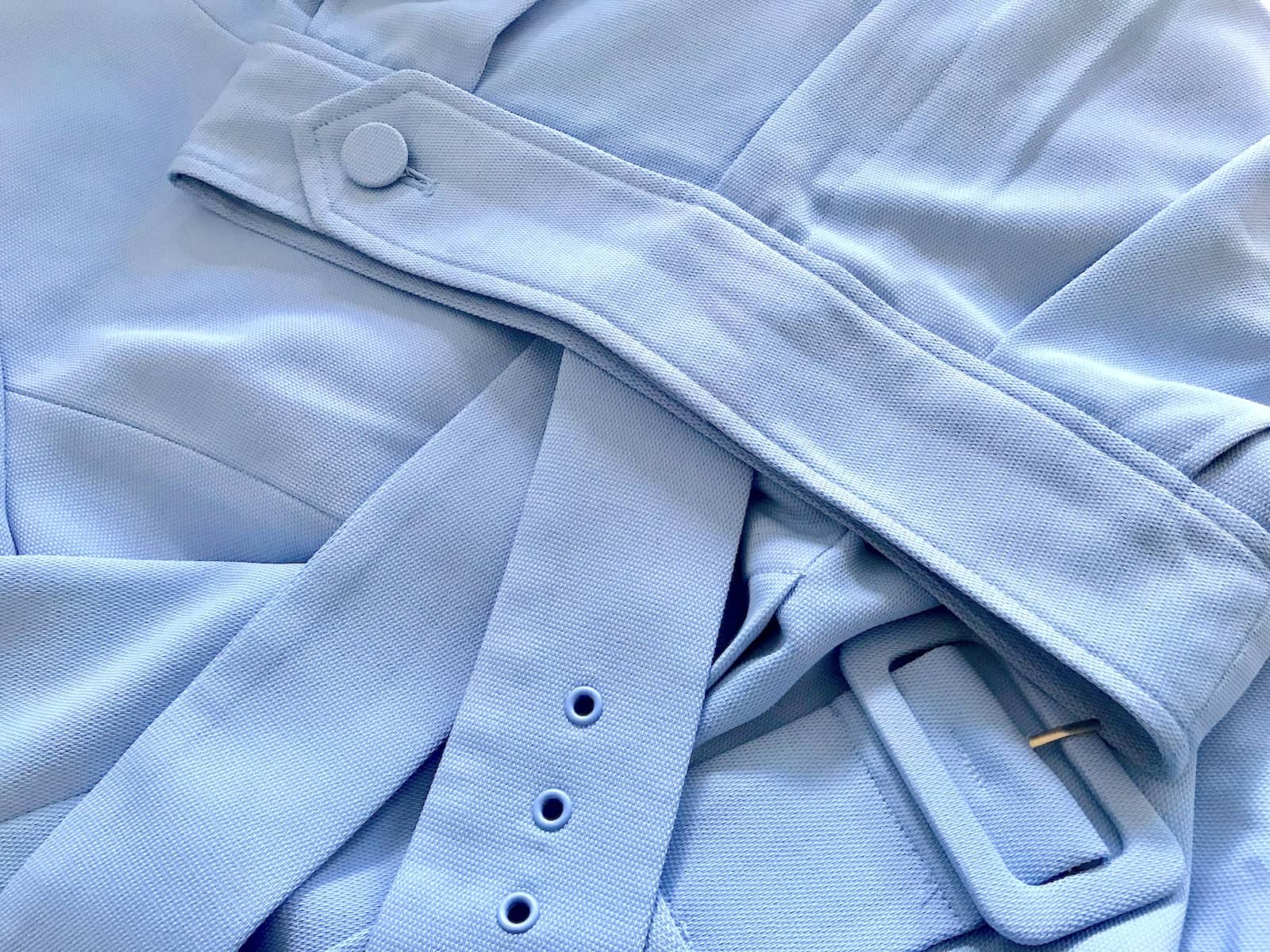 A close-up of the fabric of a pair of pants and blazer, in a cornflower blue colour. The fabric is slightly textured.