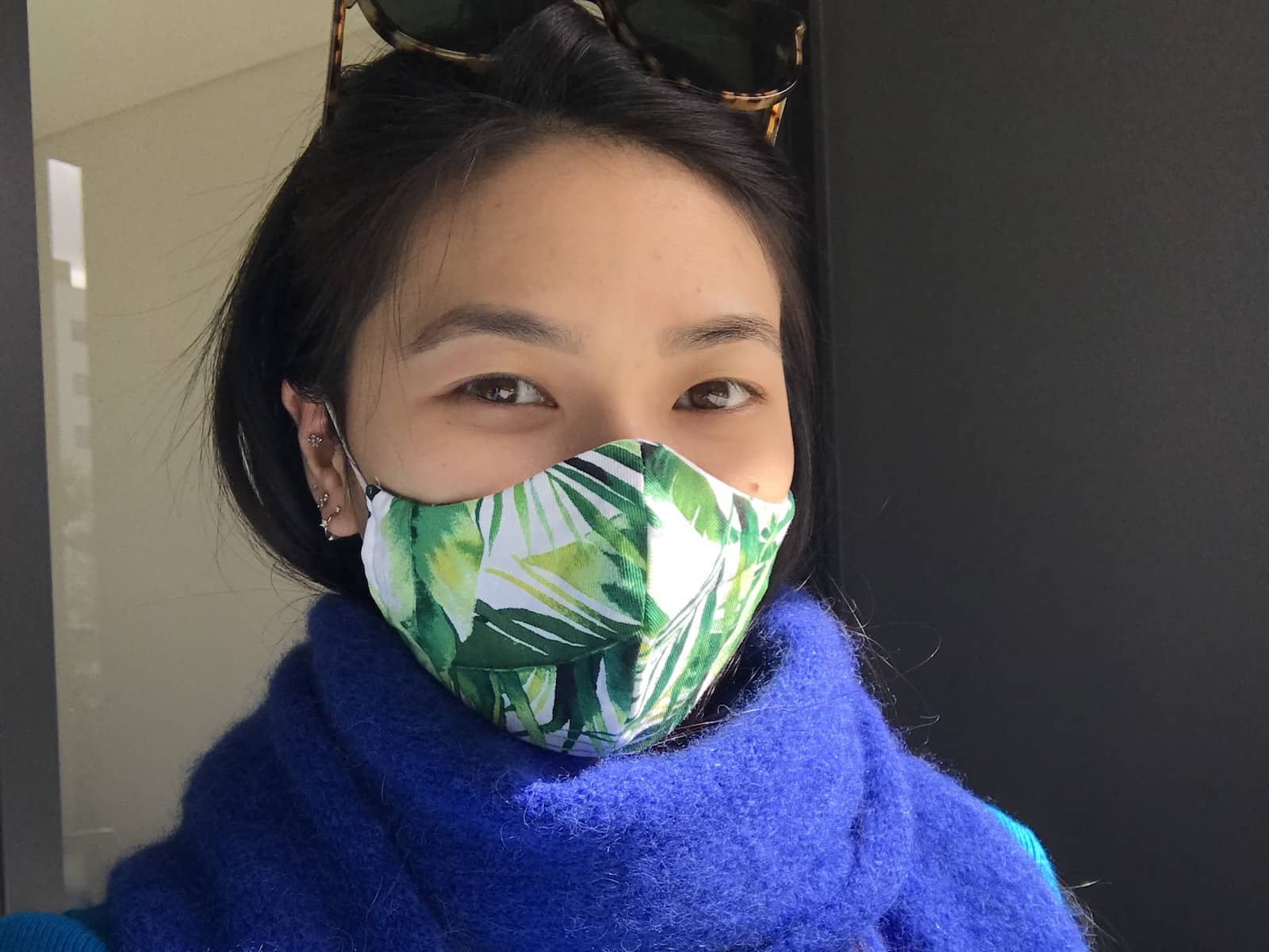 A woman with dark hair wearing a blue scarf and a white mask with green leaves printed on it