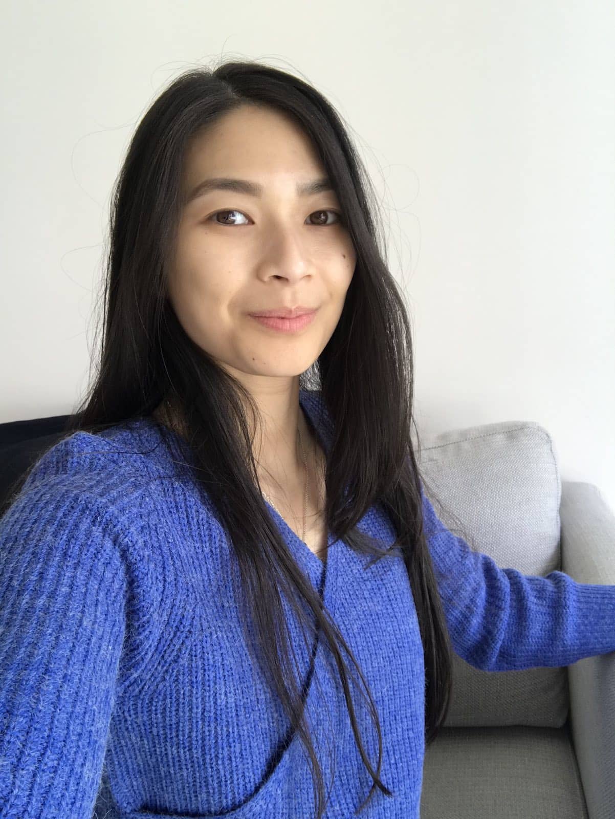 A woman with long dark hair, taking a selfie. She is wearing a blue wrap-front top in a textured knitted fabric