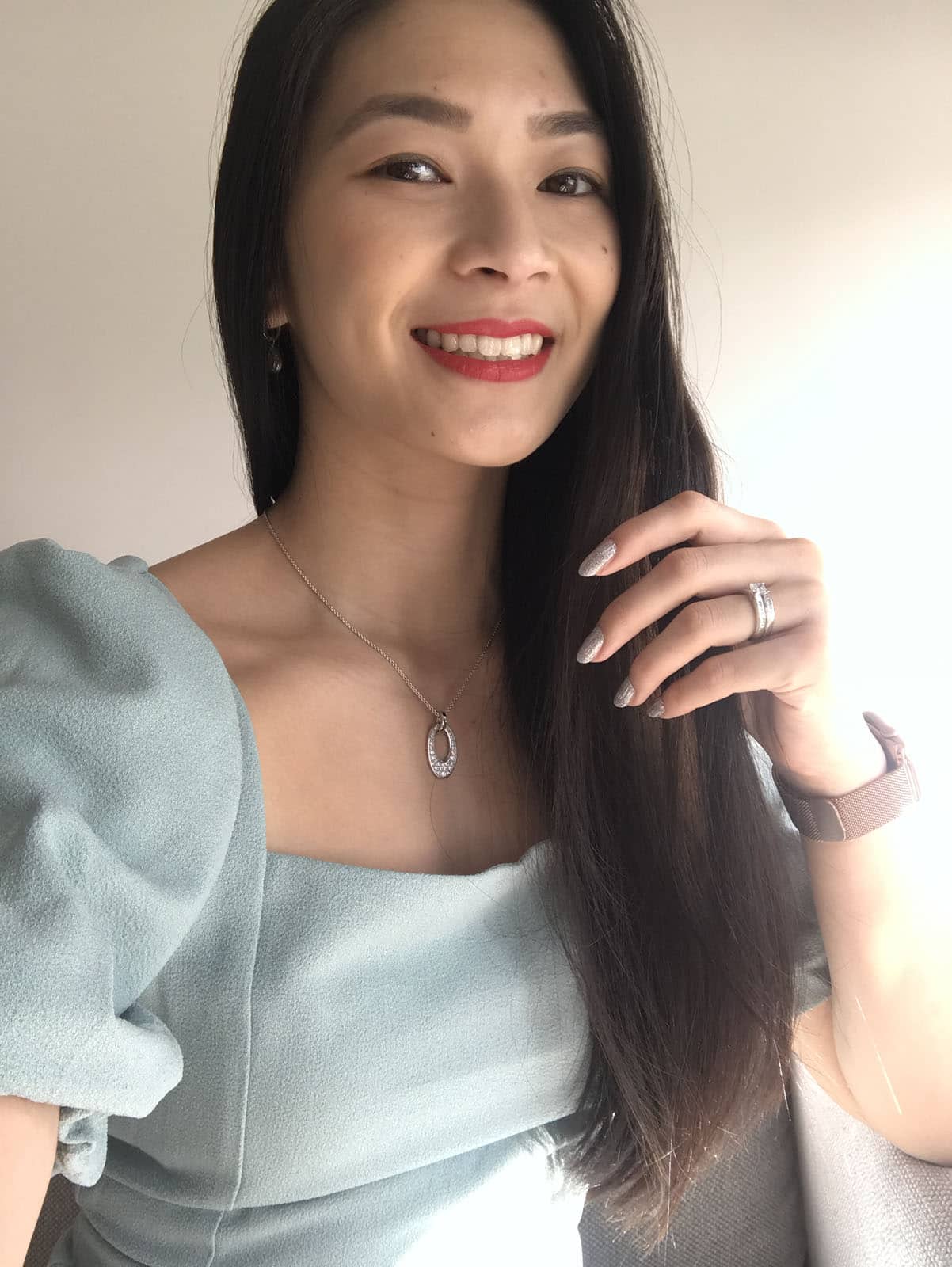 A selfie of a woman with long dark hair, wearing a light seafoam green outfit, with red lipstick on. She is also wearing silver jewellery