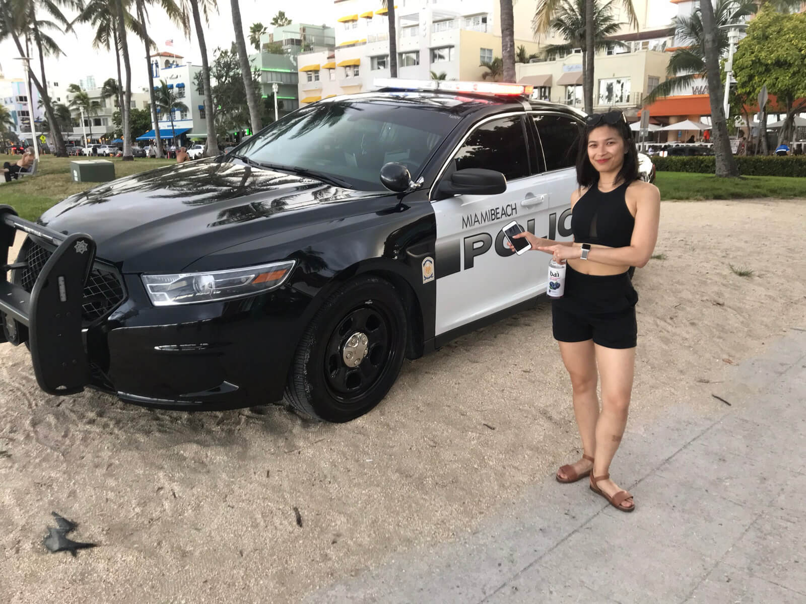 A woman in a black bikini top and black shorts, standing next to a black and white police car