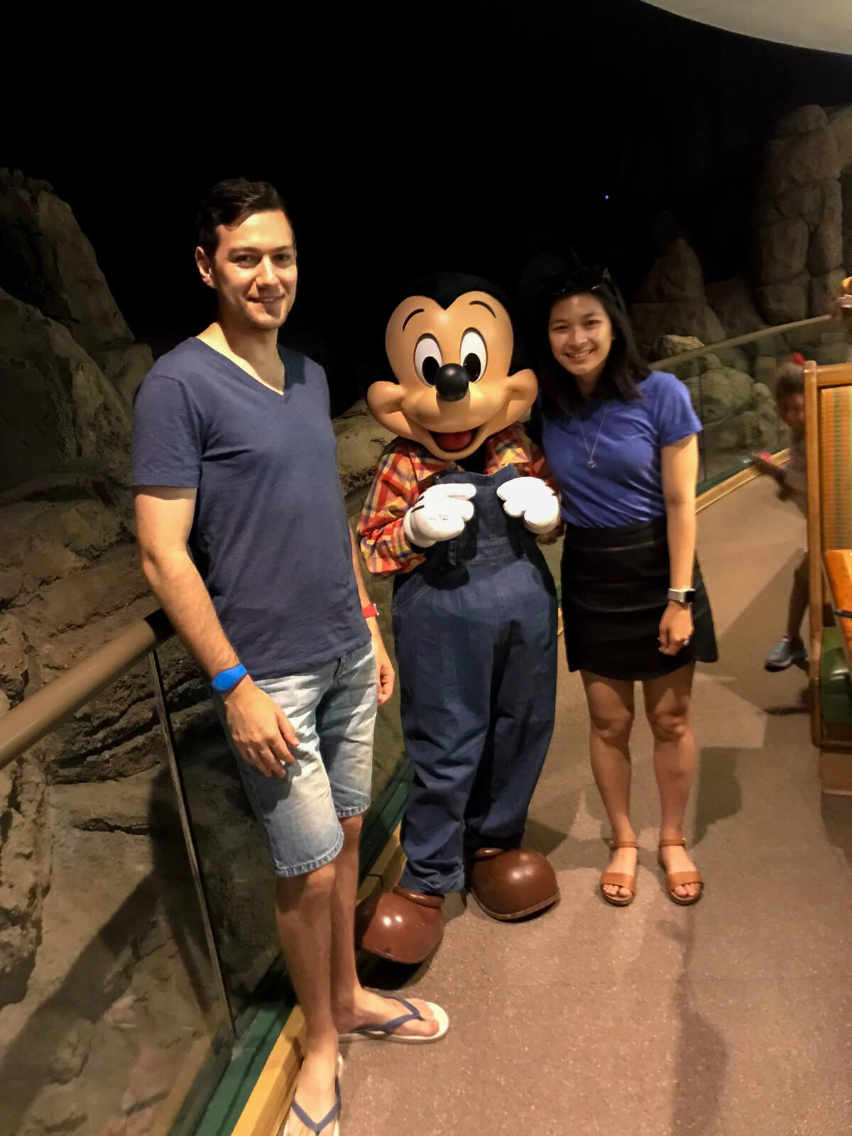 A man and woman standing alongside someone dressed as the character Mickey Mouse dressed in overalls
