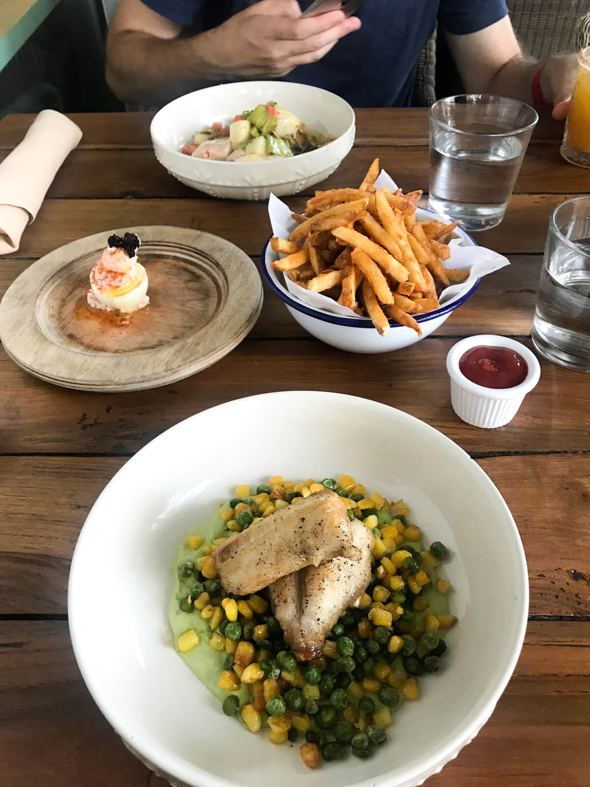 The same table with the same dishes as the previous photo, but from the opposite point of view. In the foreground is a dish with fish and carrots and peas