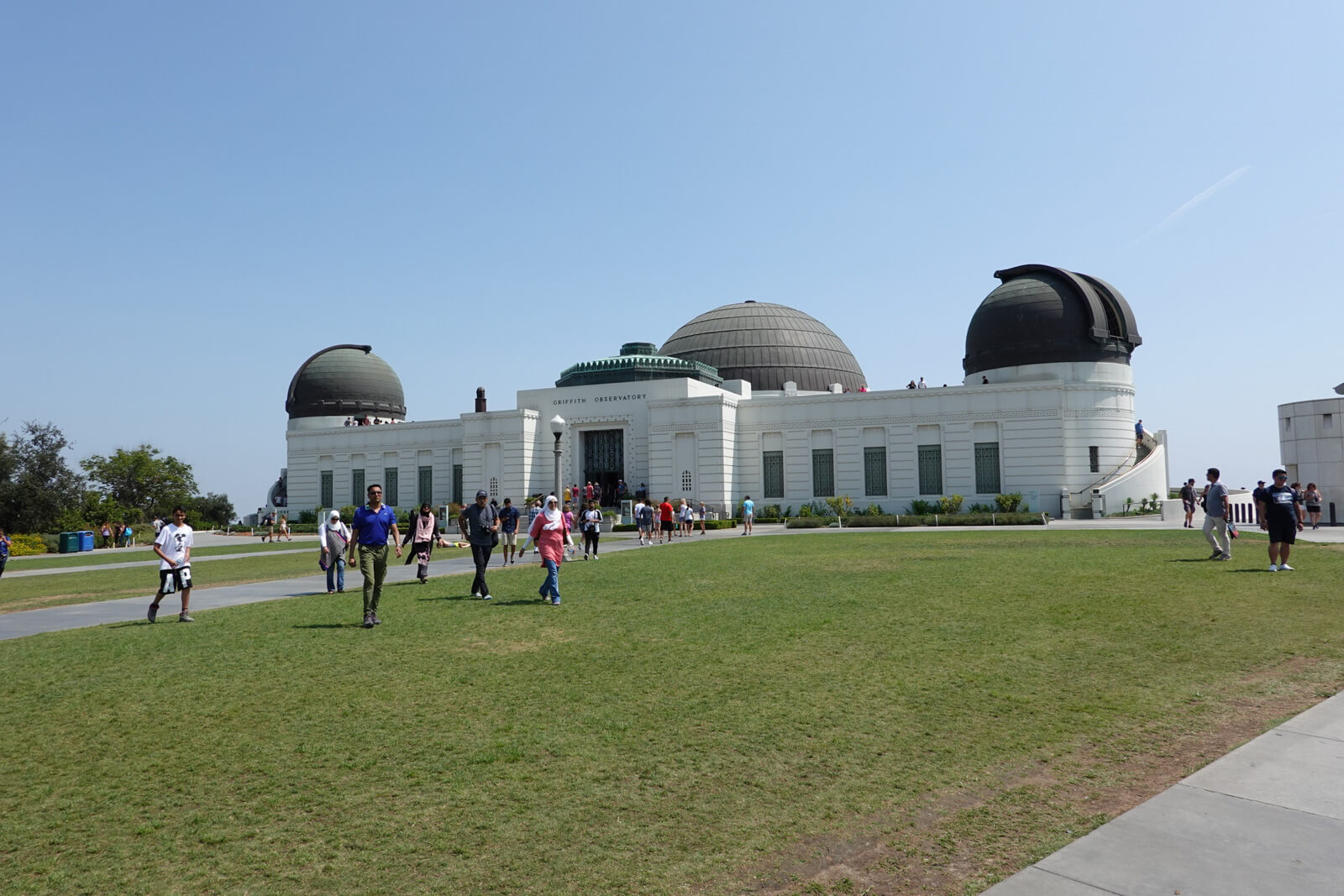 A green grassy area on an incline, with a long light-coloured building with some domes parts on top.