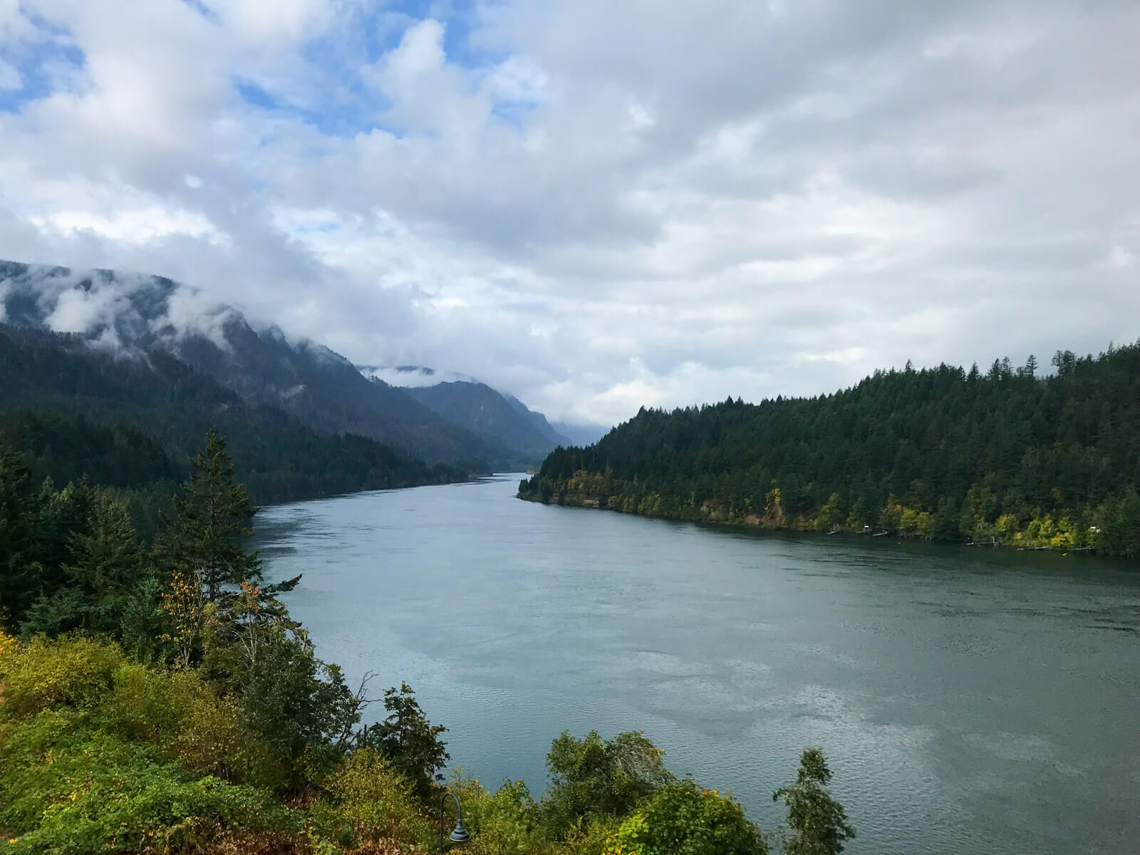 A wide river, on a very cloudy morning. There are many trees on the land by the river