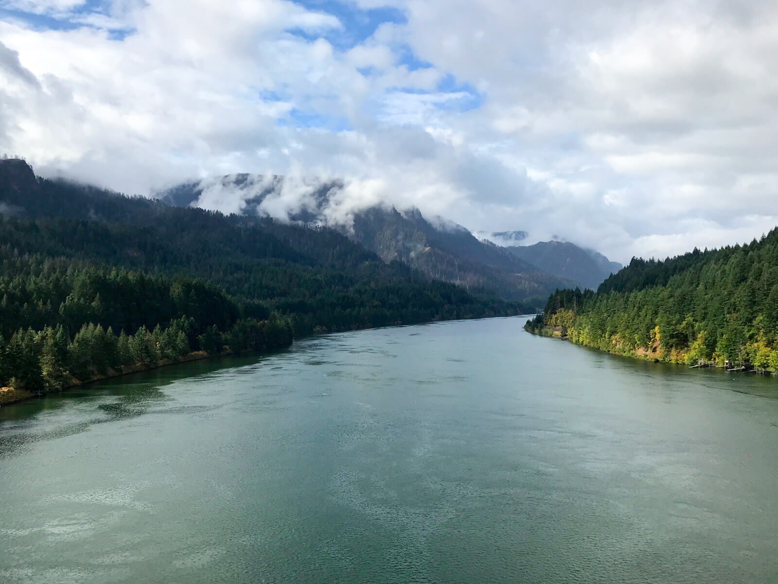 A wide river, on a very cloudy morning. There are many trees on the land by the river