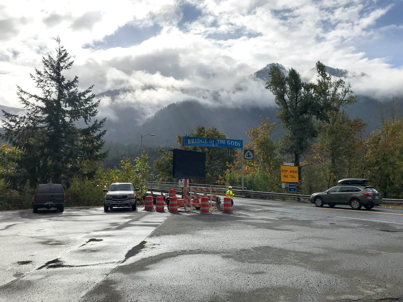 An open concrete area, like an open parking lot, with a road and the entrance to a bridge on the right. A sign above traffic height reads “Bridge of Gods”