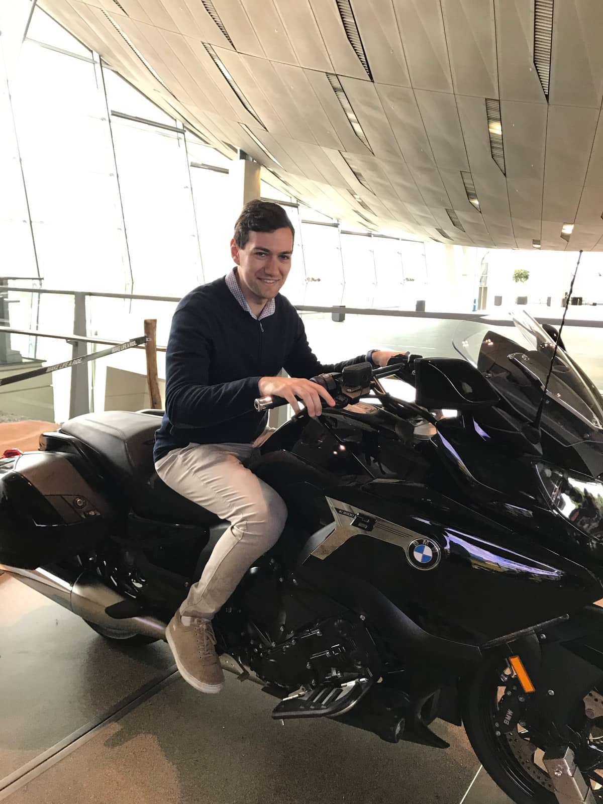 A man in a dark sweater and beige pants sitting on a motorbike in a museum