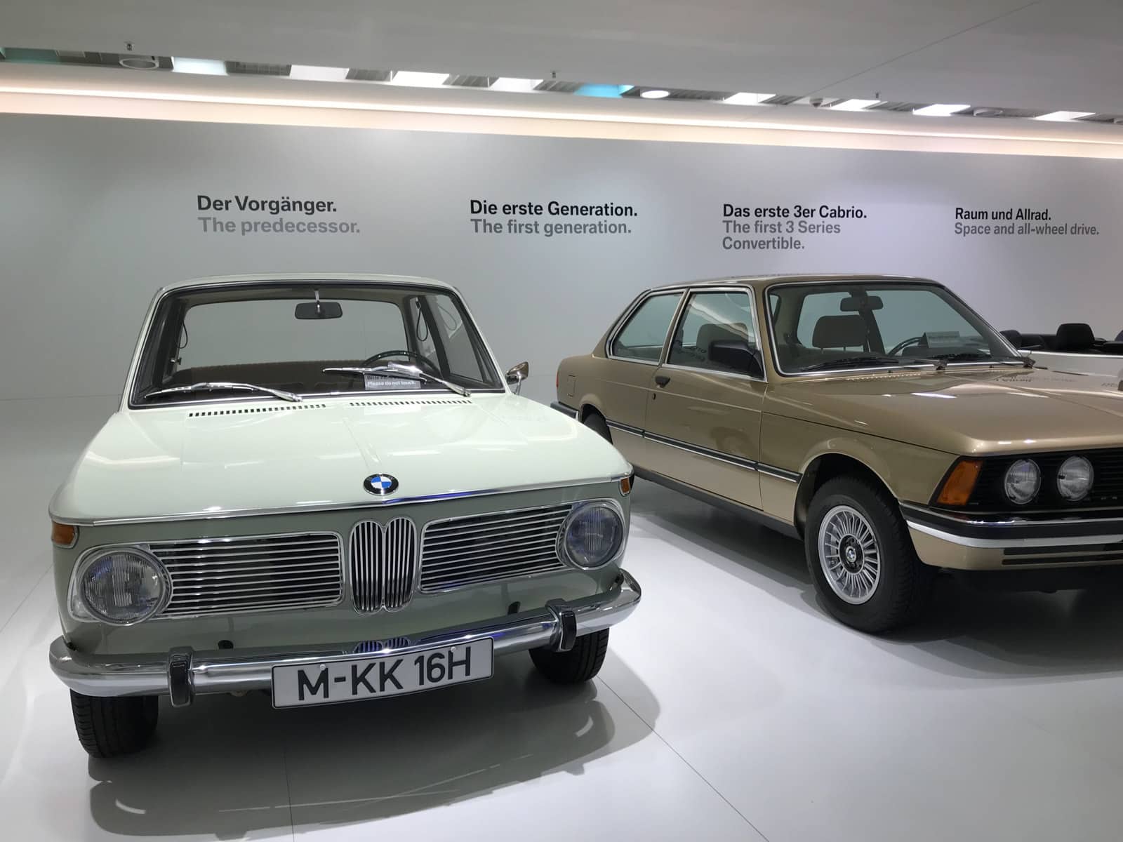 Two BMW vehicles in a museum, labelled “The predecessor” and “The first generation”.