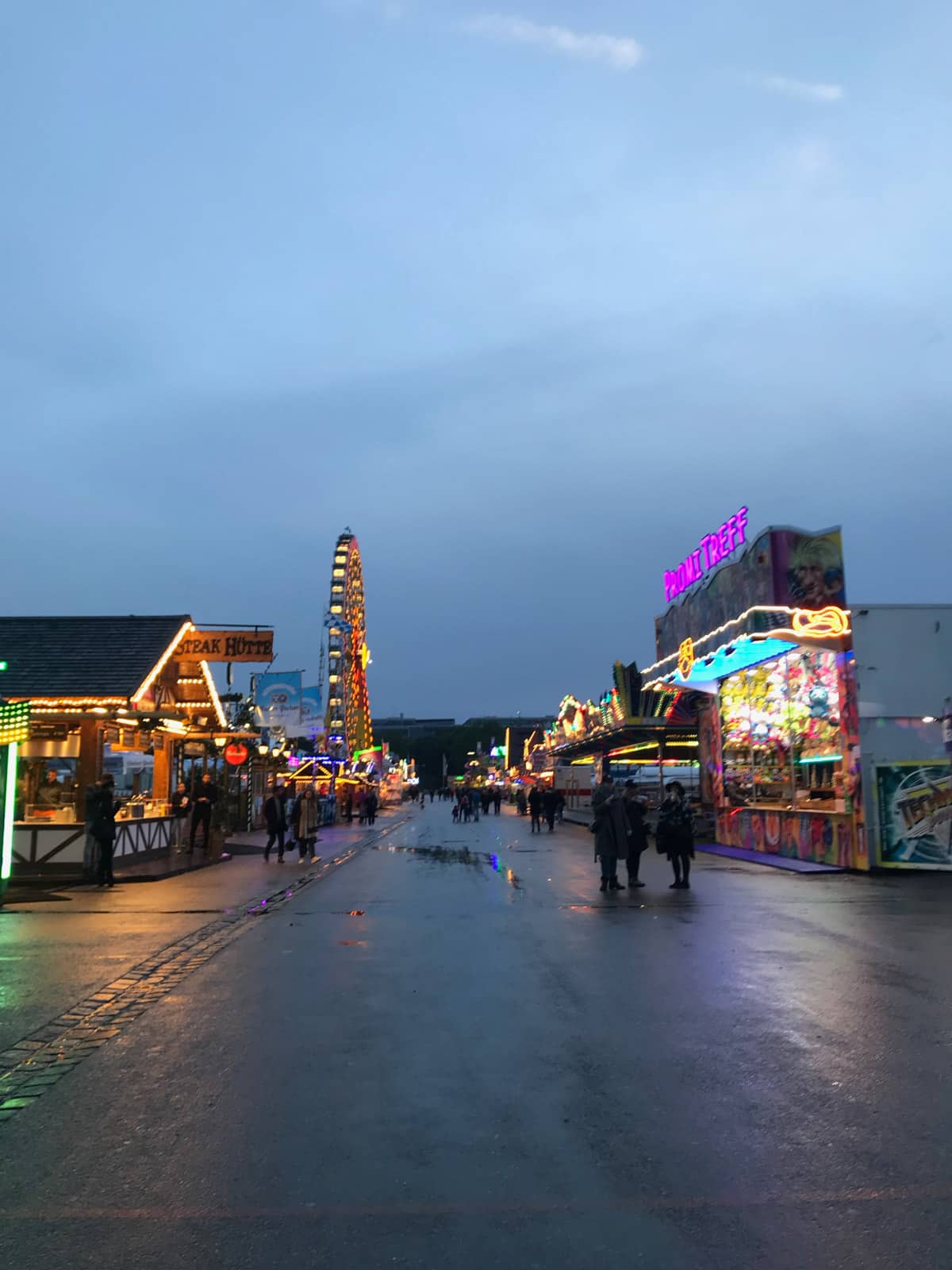 A temporary fairground area at night. The rides have their lights on.