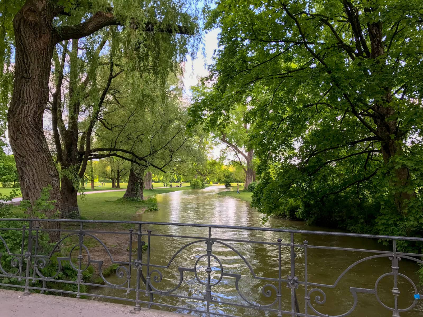 A river inside a park, seen from a small bridge going over the river. The greenery is very lush