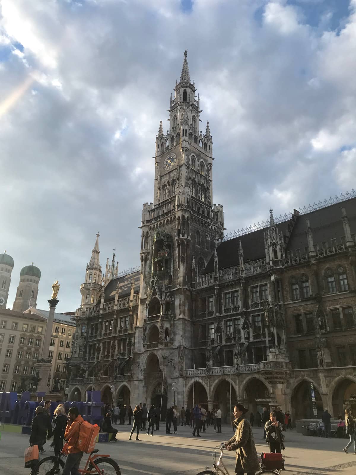 An old tower in downtown Munich, characterised by its old architecture. In the foreground are people taking photos and riding bicycles