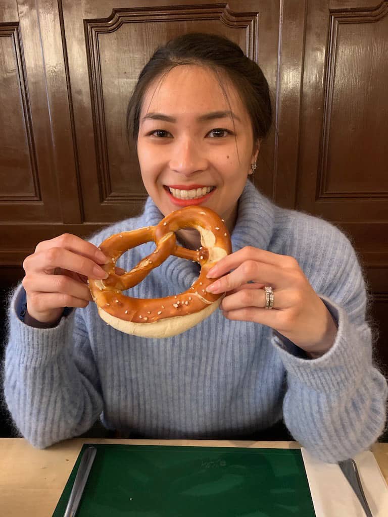 A woman with a light blue sweater holding a soft pretzel and smiling