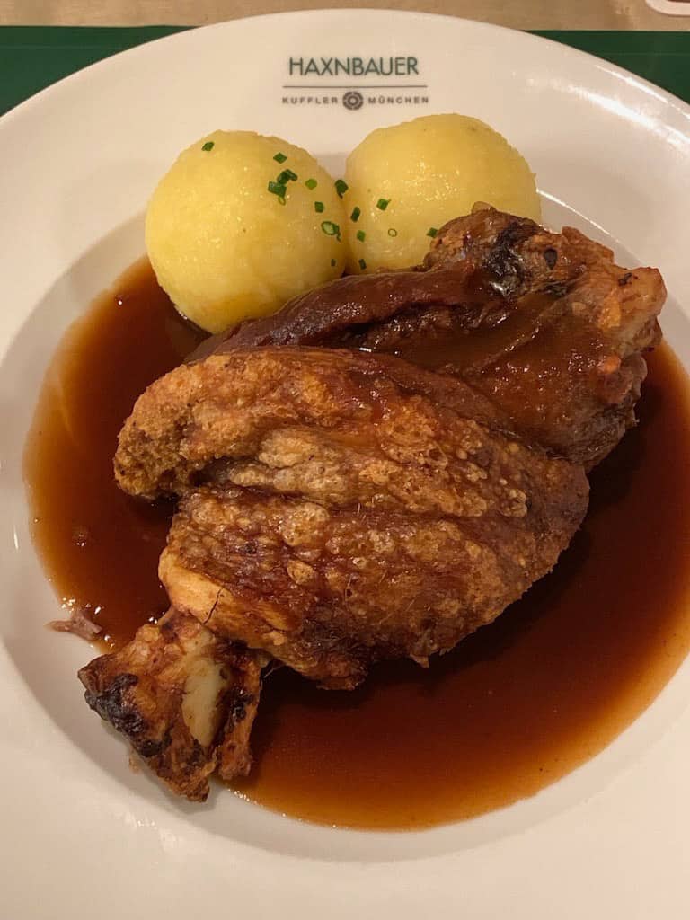 A plate with a serving of pork knuckle and sauce, with two round potato dumplings