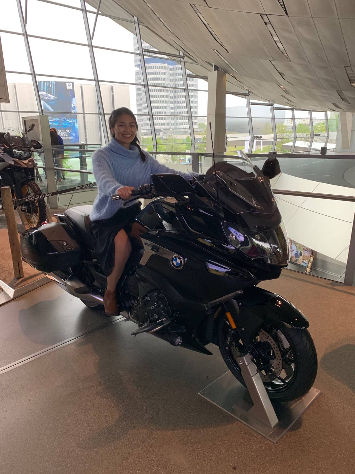 A woman wearing a blue sweater sitting on a motorbike in a museum