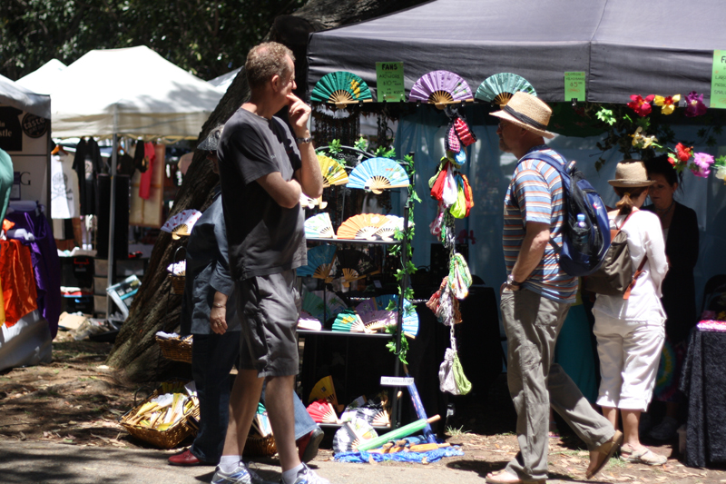 People walking past a stall with some paper fans