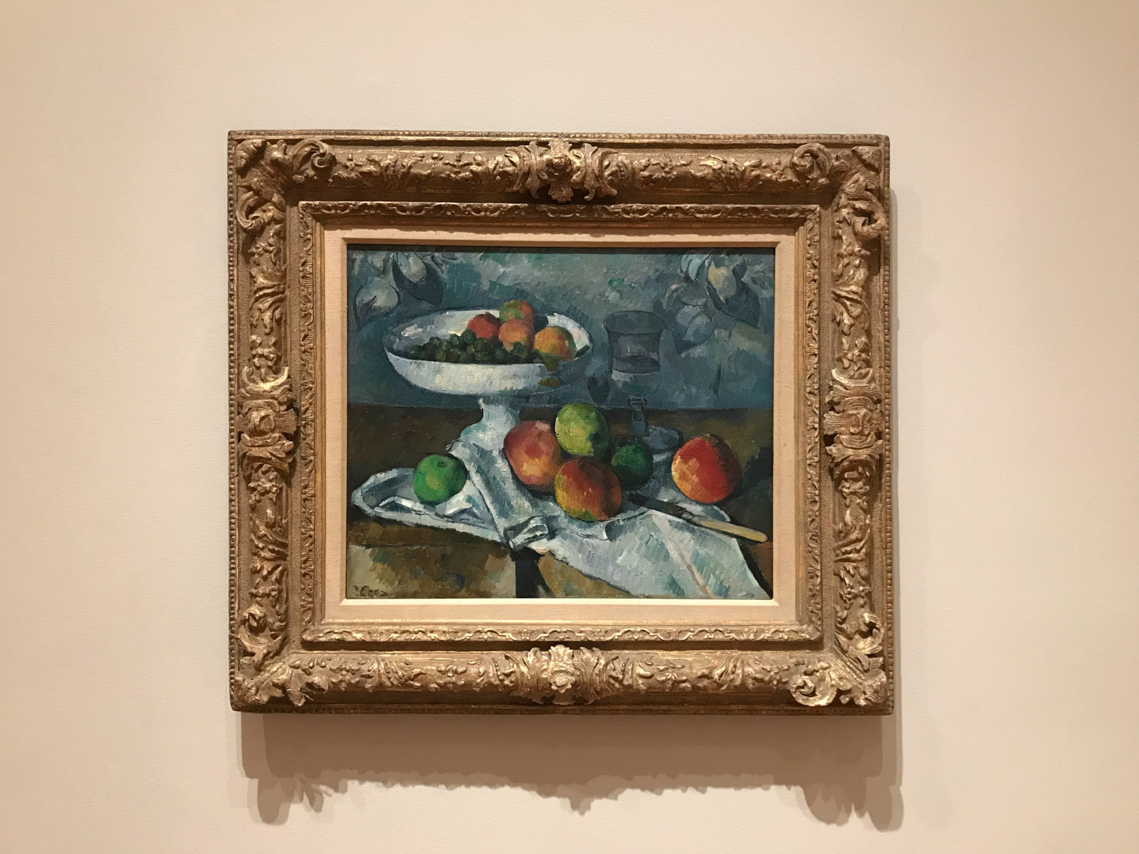 A framed painting of a bowl of apples, with some apples on the surface underneath