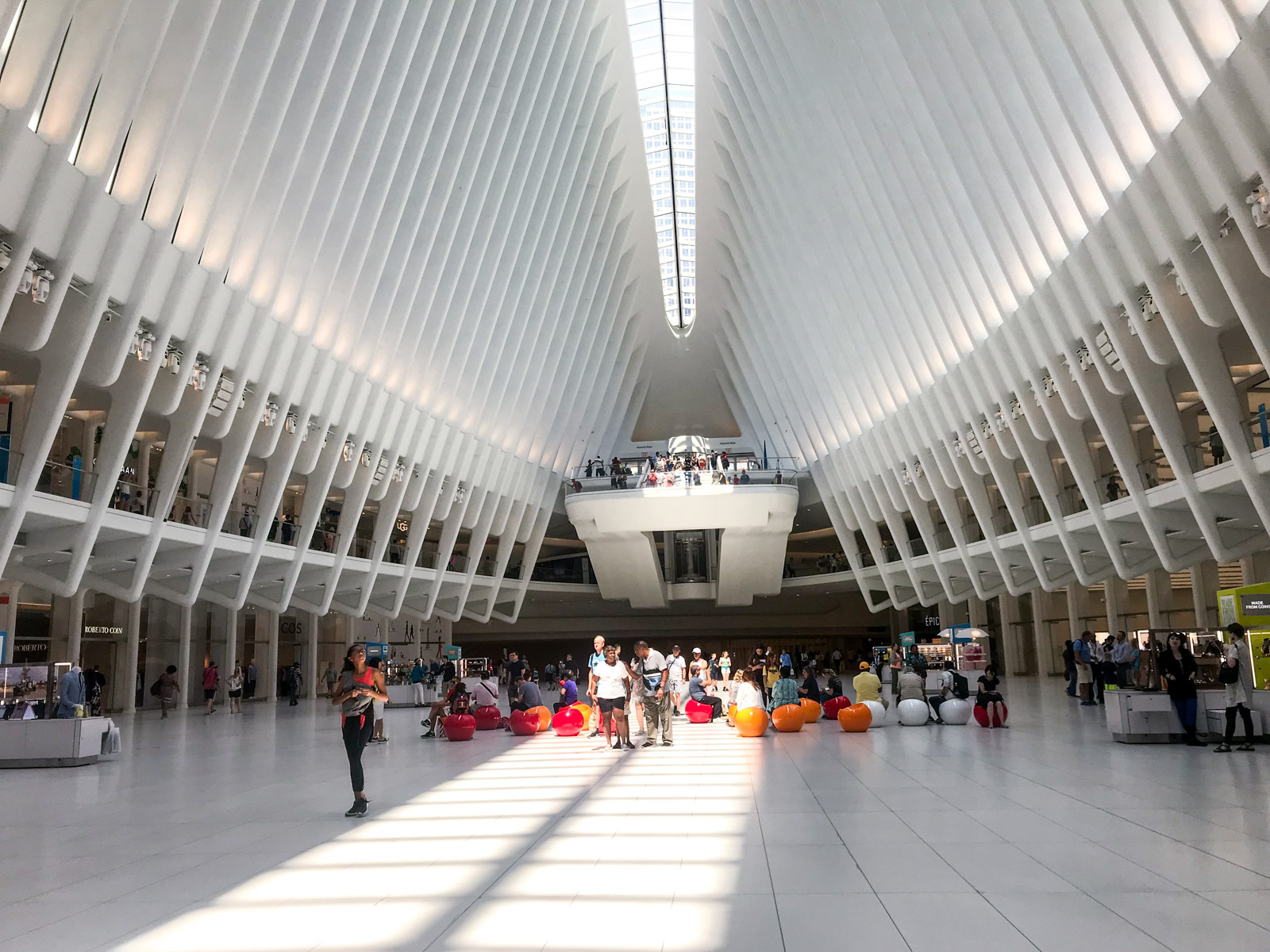 The inside of a white building with white panels from the sunlight roof and down the sides. Sunlight flows through the glass windows at the top