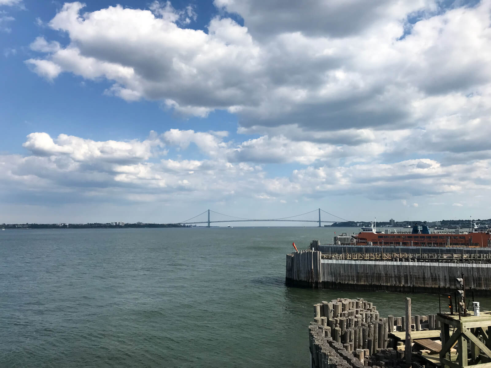 A long bridge connecting two parts of land, seen from afar. In the foreground is a small wooden dock and a small boat