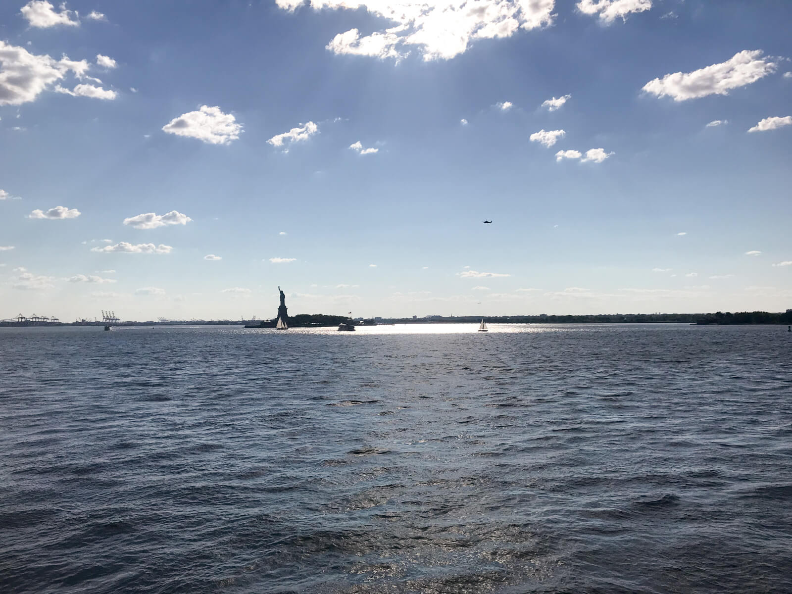 The Statue of Liberty as seen from a ferry on the water. There is little sunlight as the sun has moved behind the clouds