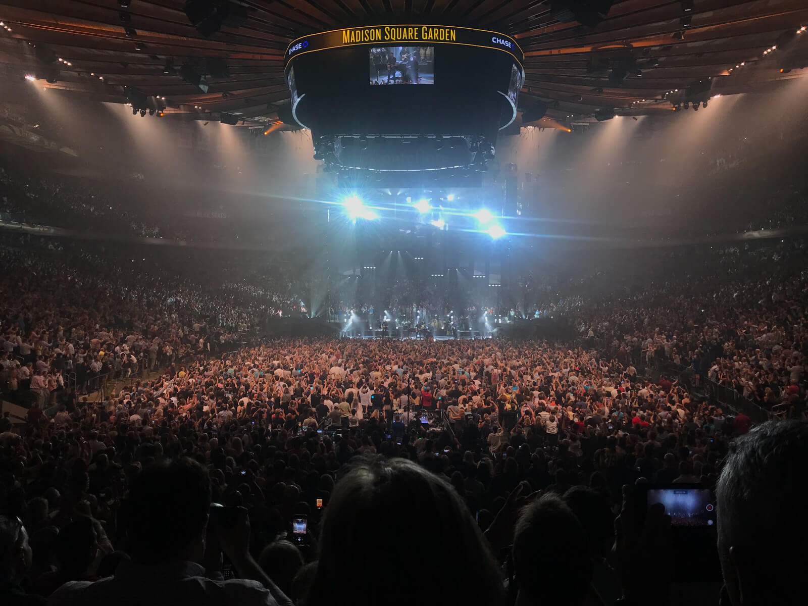 Another, differently-lit view in the same scene as the previous photo, showing a large amount of audience members standing in front of a large area in front of the stage