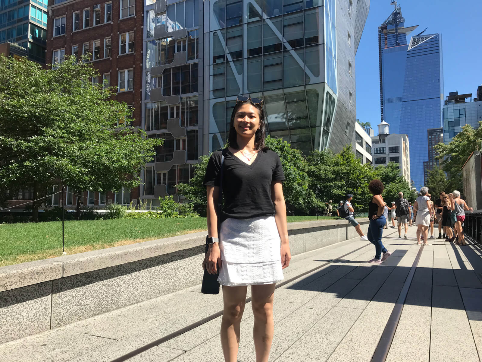 A woman standing on a refurbished train line, with both modern and old buildings in the background. She’s wearing a black t-shirt and a white skirt