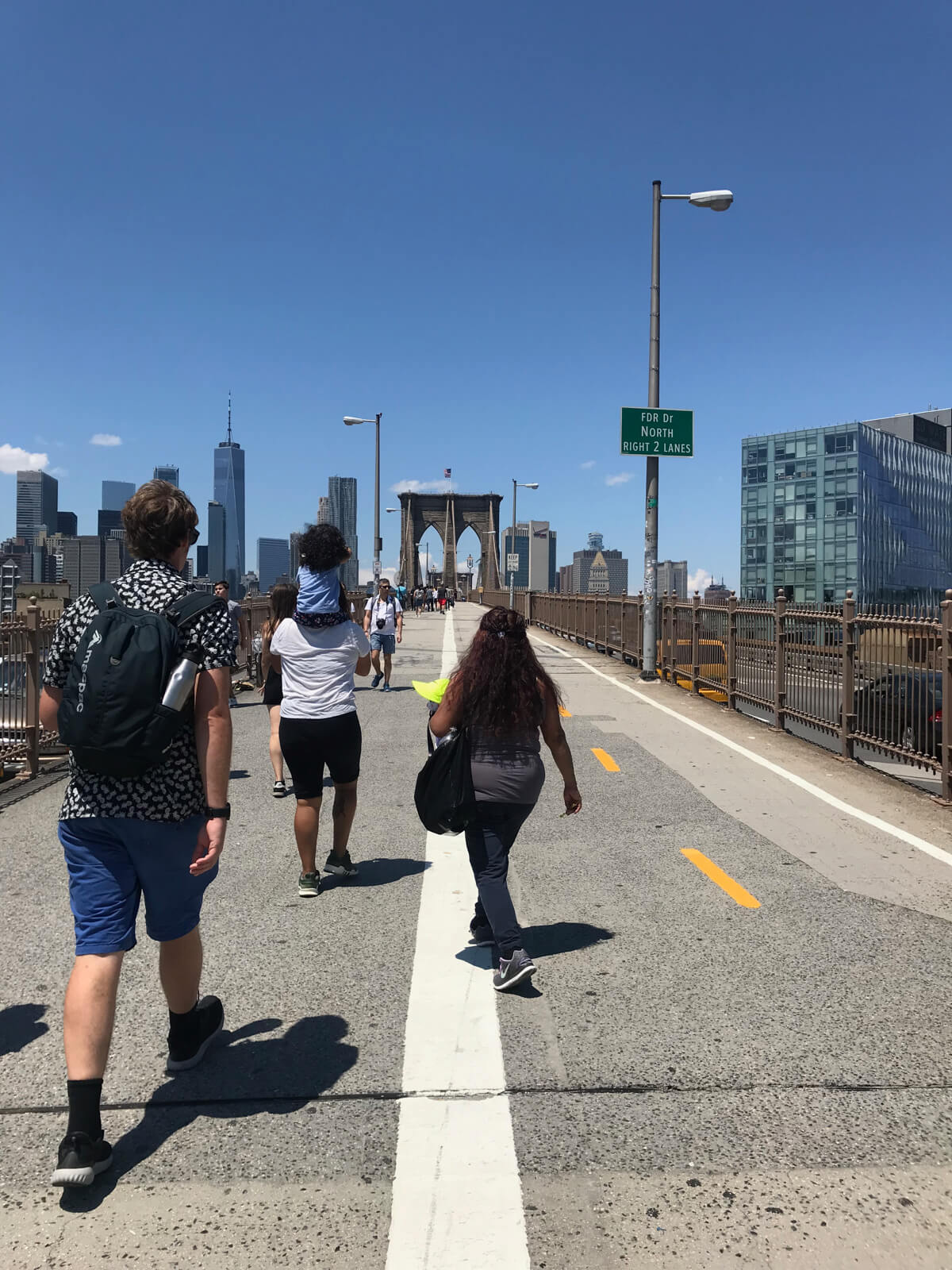 Some people approaching a road leading to a bridge. In the background are some high-rise buildings
