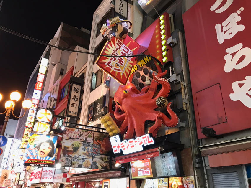 A squid sculpture in the background, displayed above one of the takoyaki (squid balls) stores
