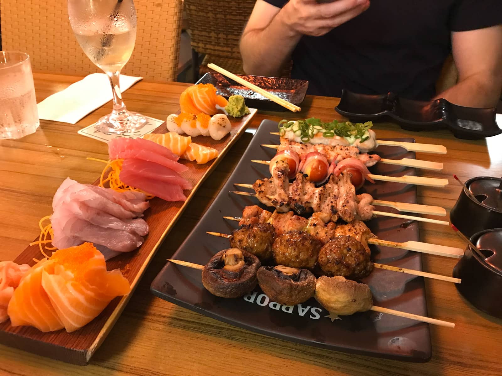 A restaurant table with a plate of small skewers of meat, and sliced raw fish on a separate plate