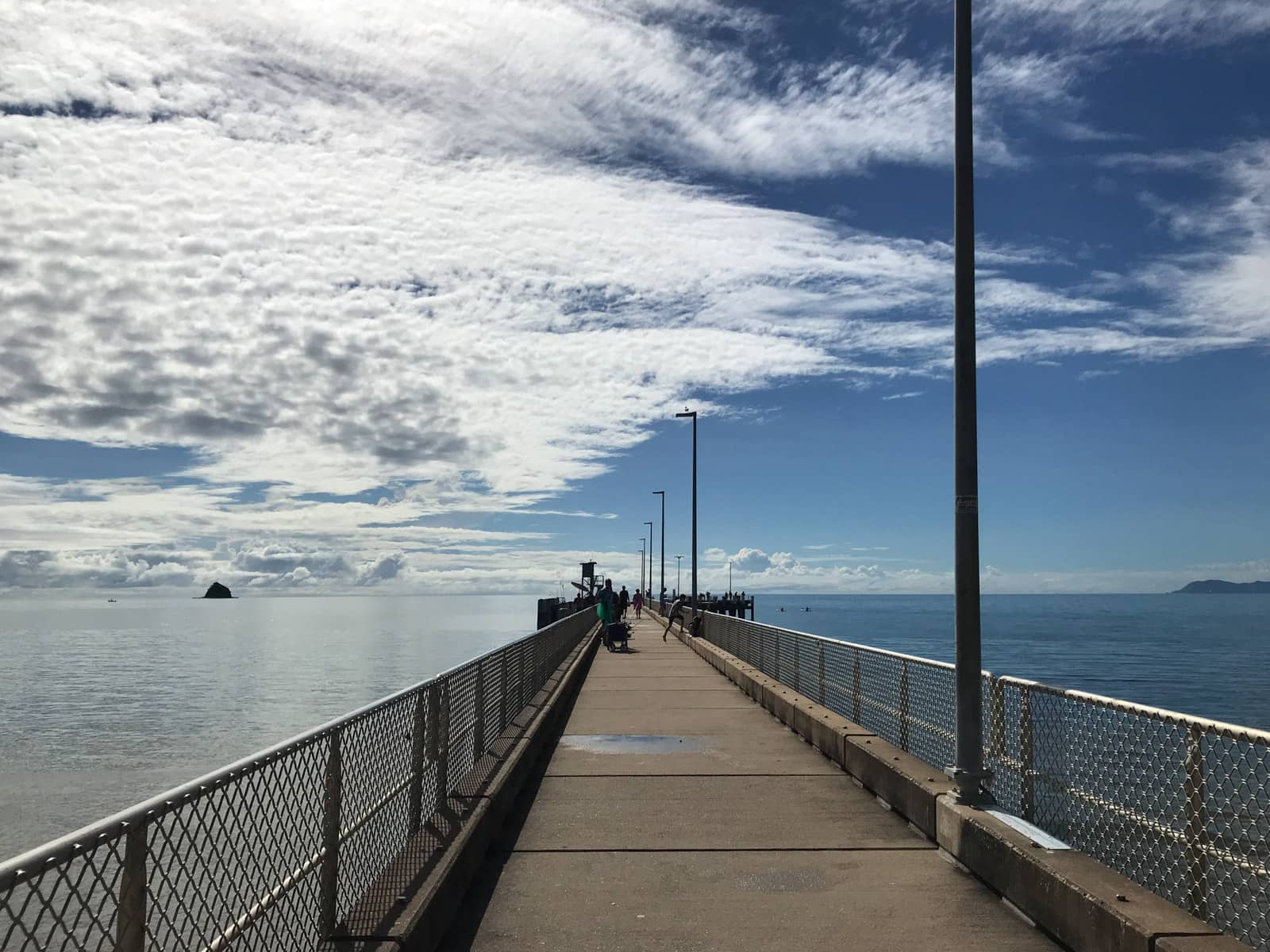 A view along a boardwalk, over the ocean. It’s a bright day and clouds are stretched across the sky