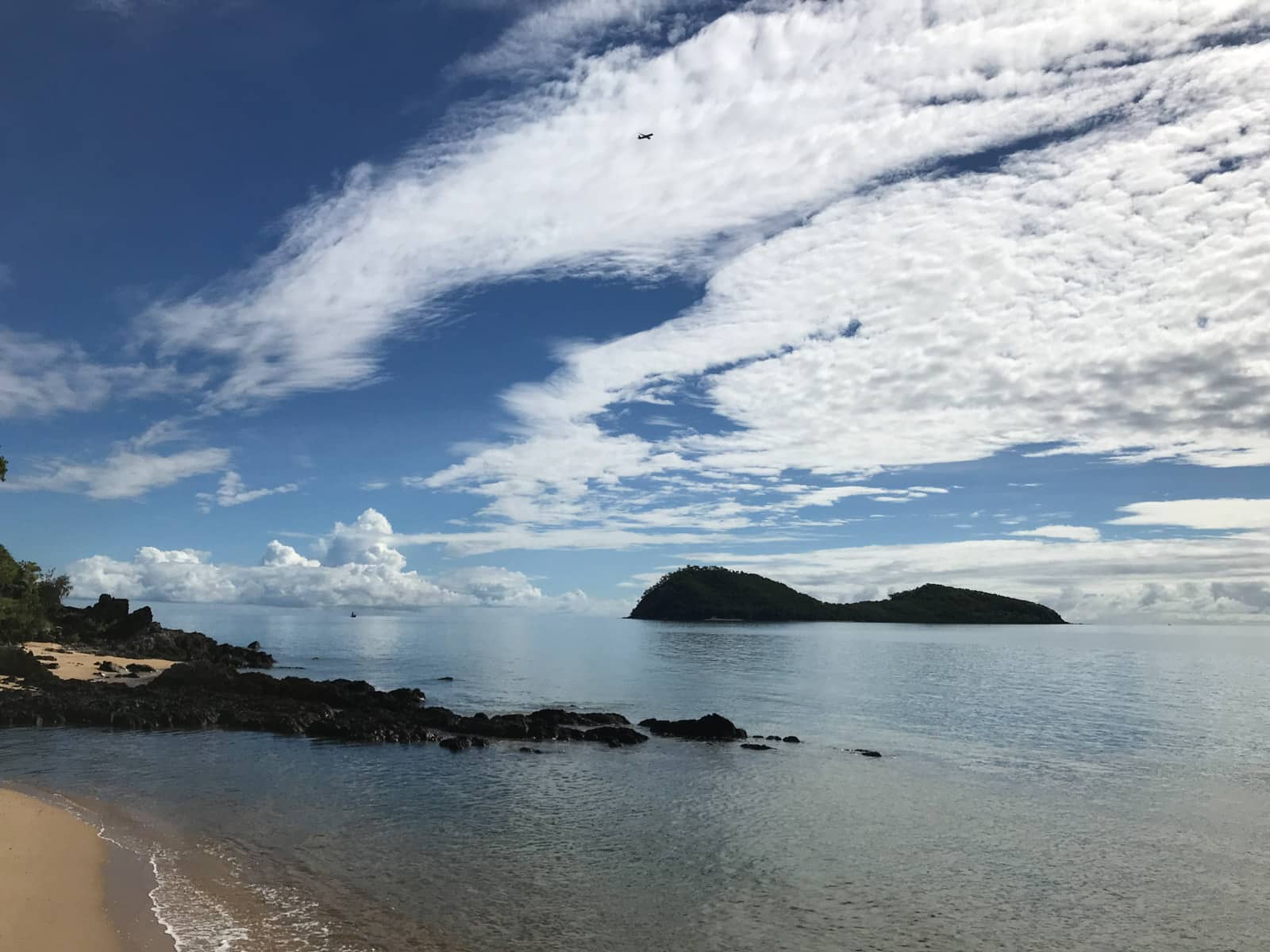 A view of the ocean with part of the sand at the shore visible. There is a large island in the distance that seems to be covered with trees