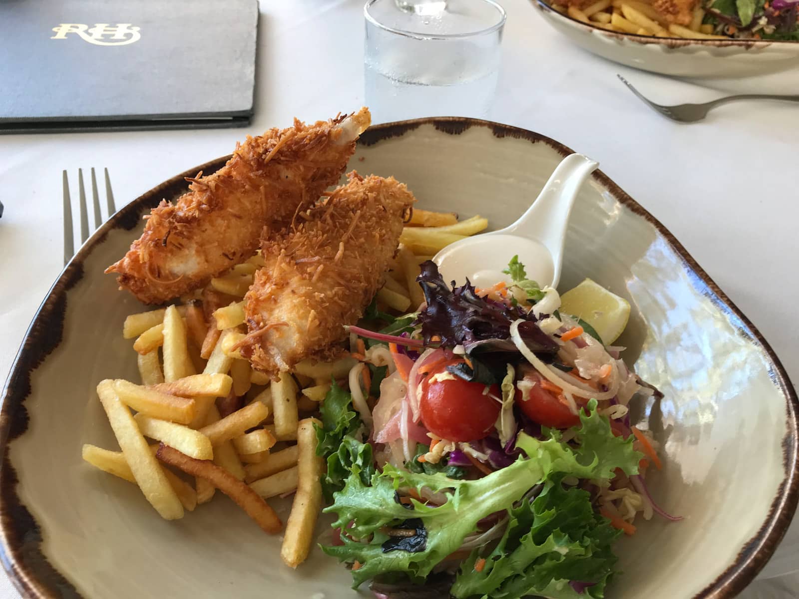 An irregular shaped bowl with some fries, garden salad and battered fish.