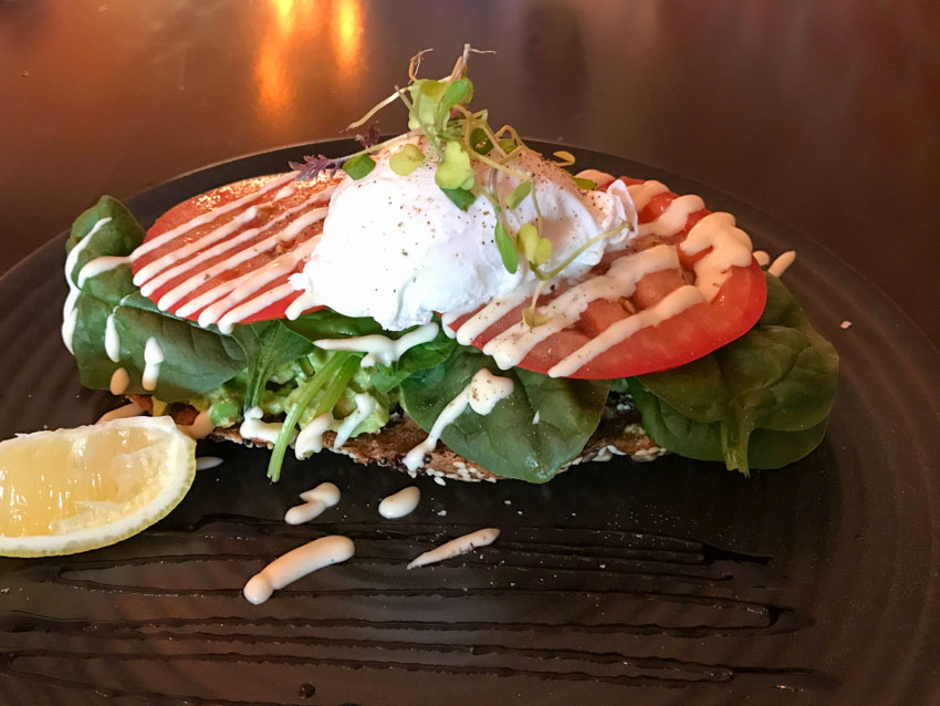 Sliced tomatoes along with avocado and a poached egg on toast