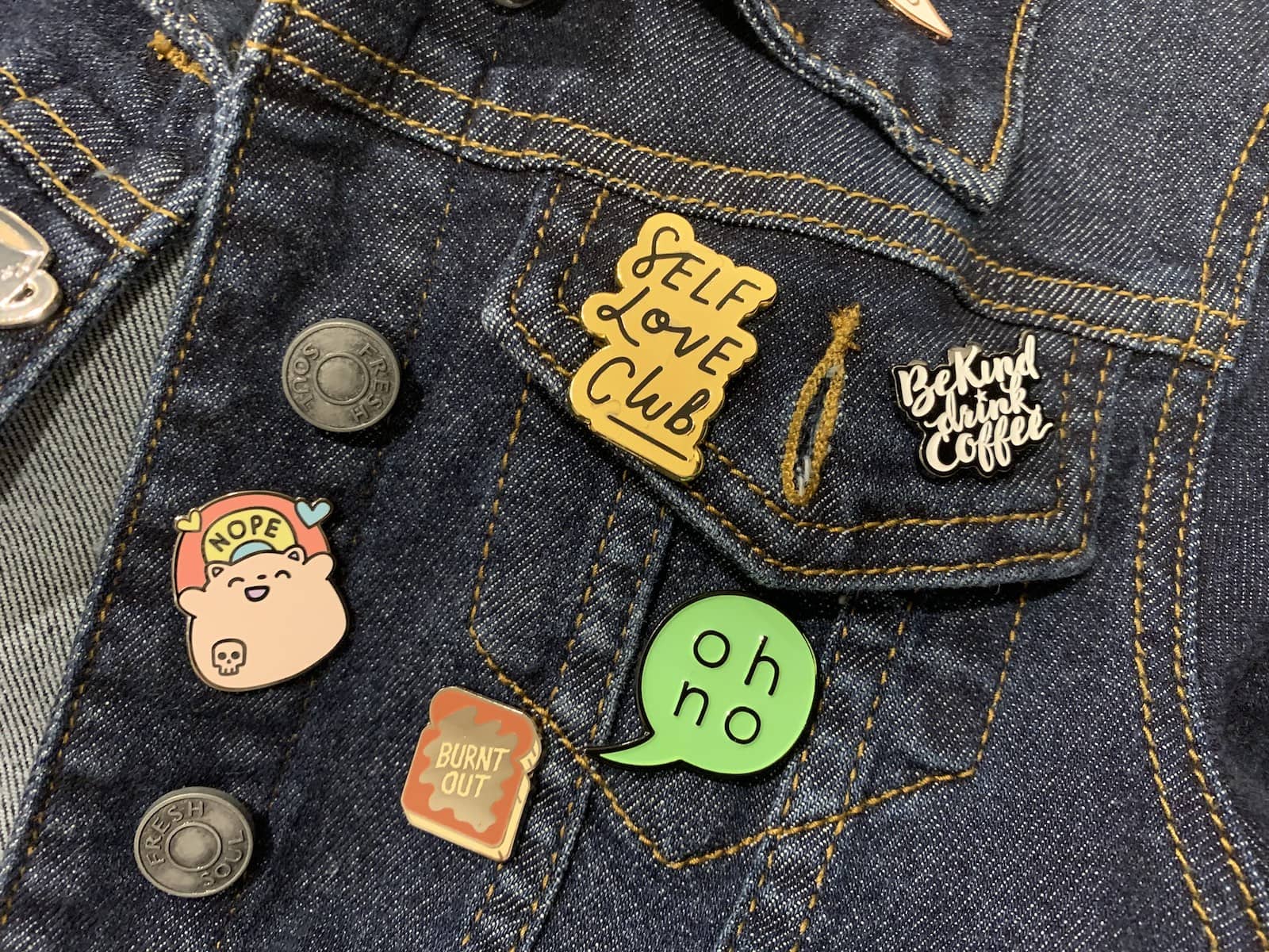 Part of a dark denim jacket with a few enamel pins on it