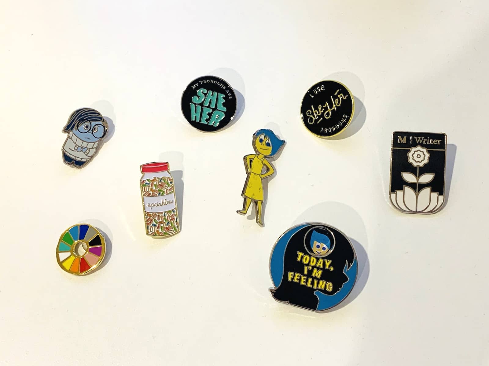 A handful of enamel pins on a flat white surface.