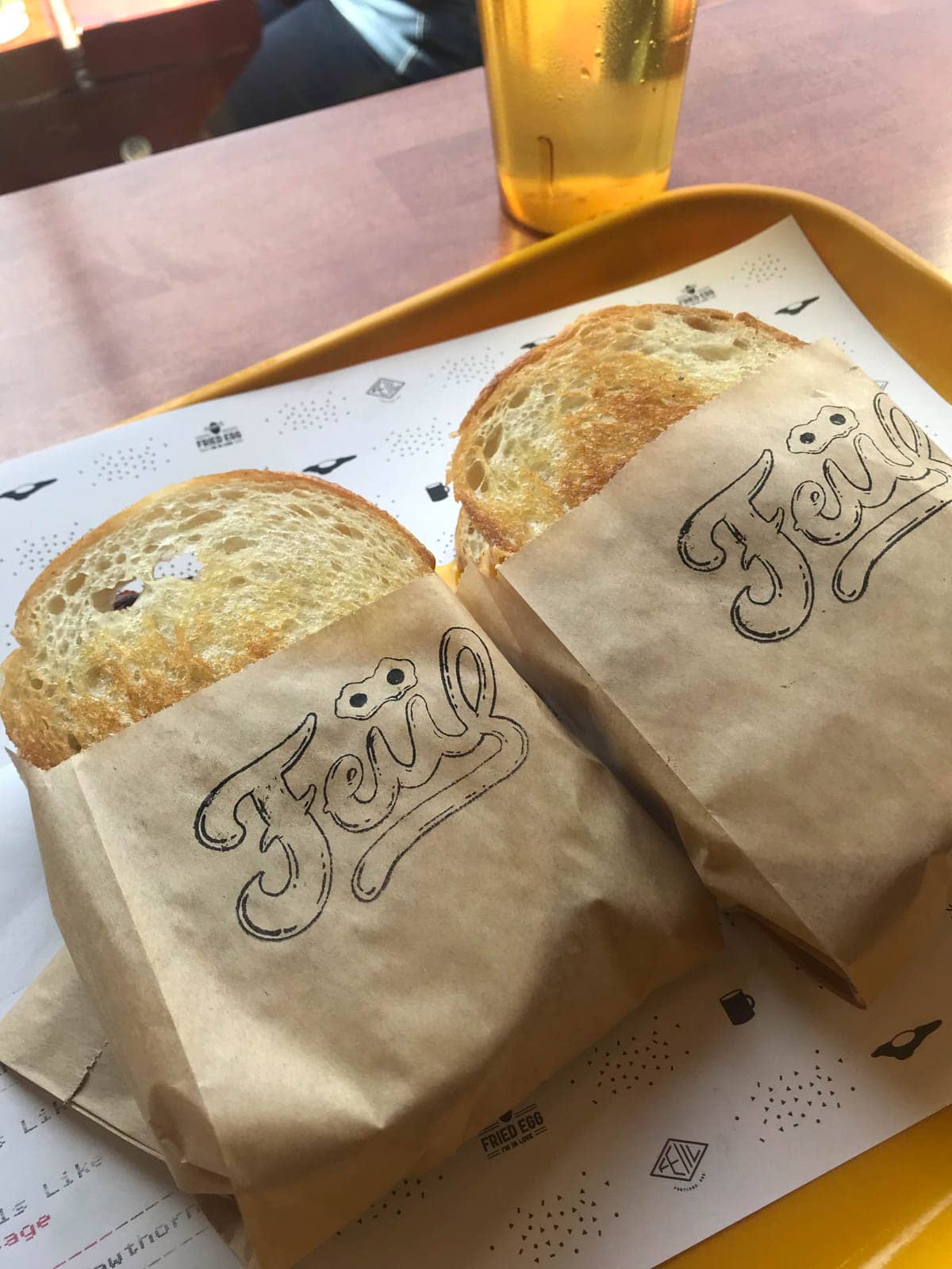 Two toasted egg sandwiches wrapped in brown paper, sitting on a yellow tray.