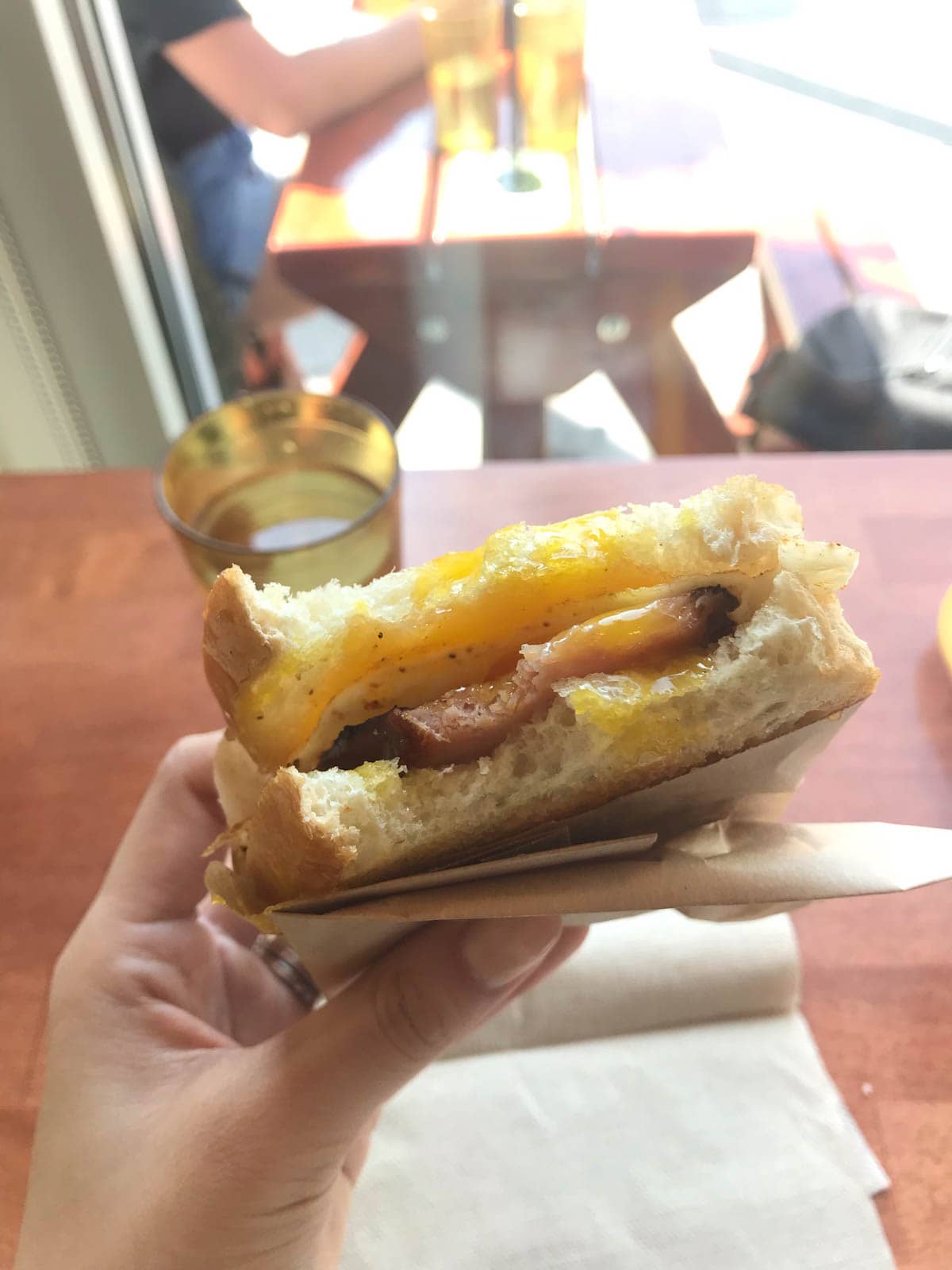 A toasted egg sandwich, bitten into, in a woman’s hand.